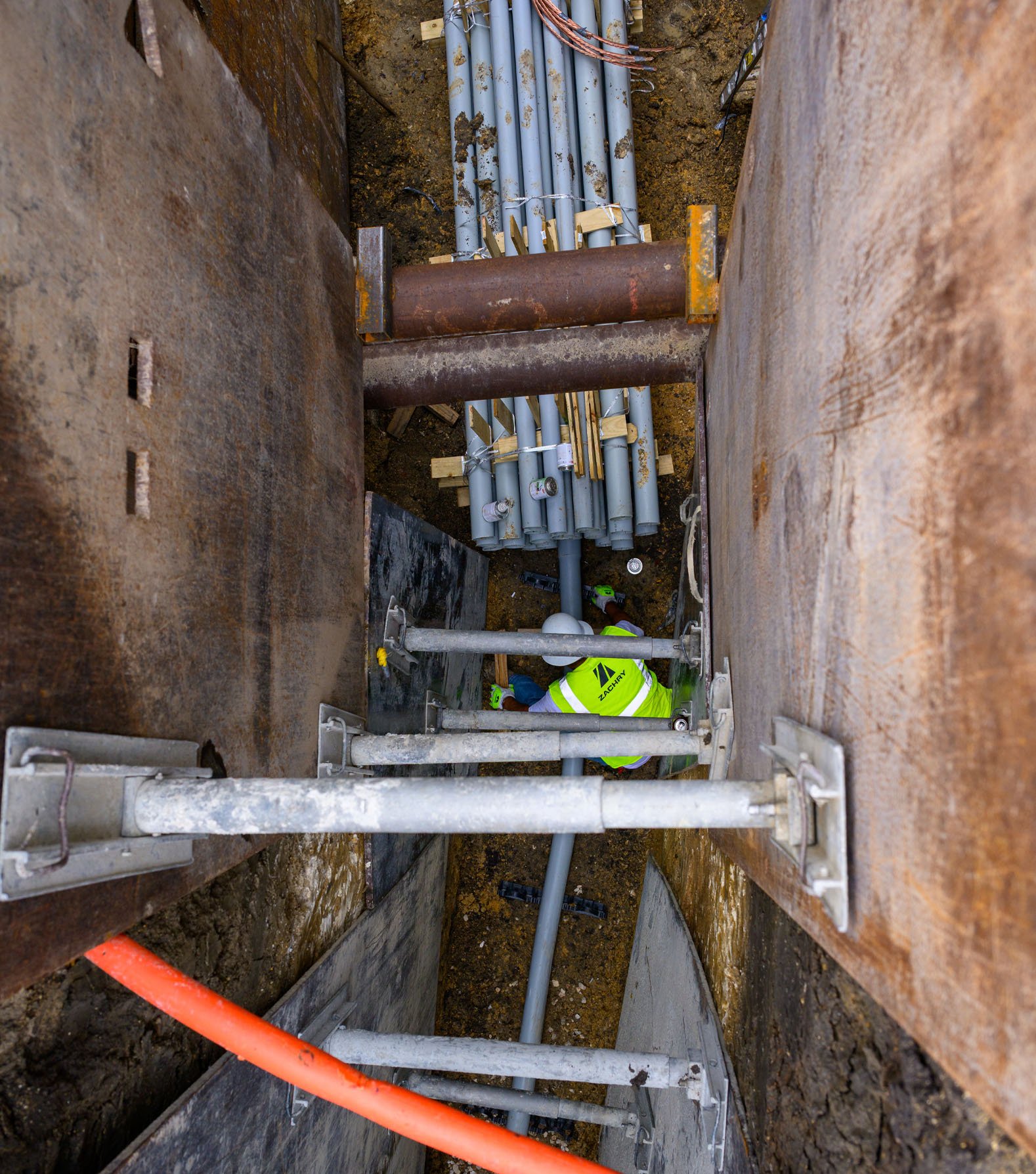 Top view of worker installing utility conduits inside a shored trench
