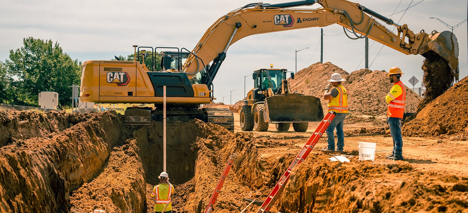 Construction crews and heavy equipment working alongside an excavated utility trench