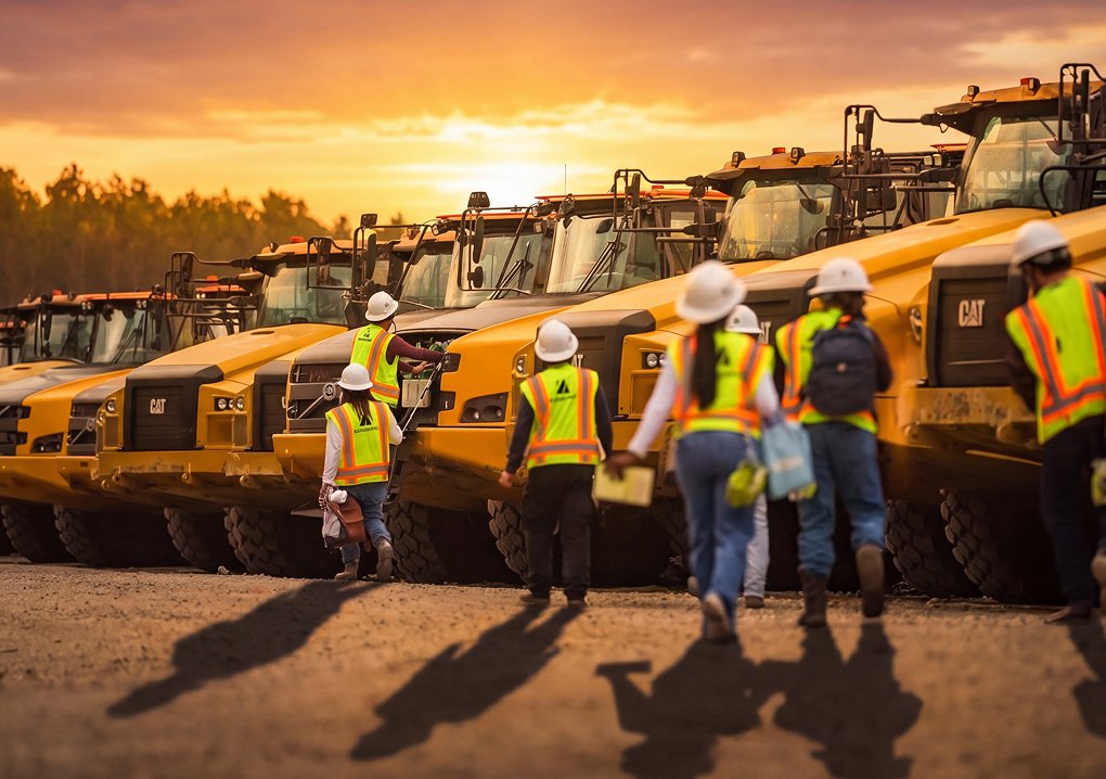 Zachry team members walking toward a fleet of heavy construction equipment at dawn